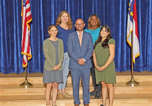 Office Staff on the steps of the stage against a blue curtain with flags